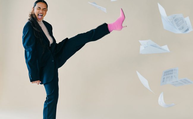 Studio shot of a young woman screaming while kicking a paperwork into the air against a brown background